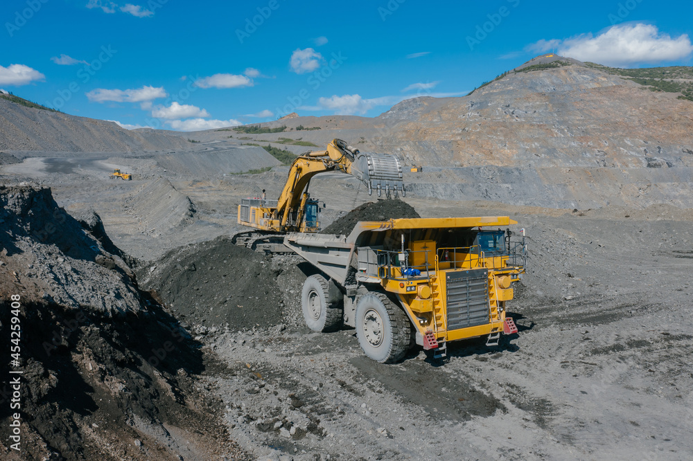 An excavator loads ore into a dump truck. The action takes place in an open pit.