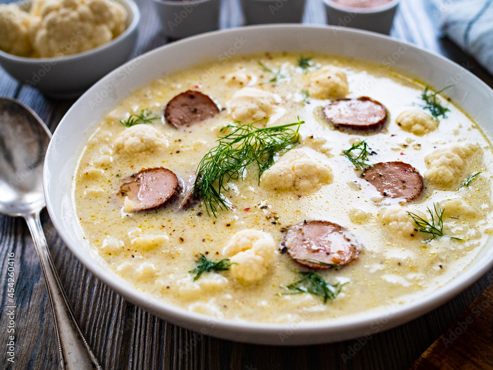 Cauliflower soup with sausages on wooden table
