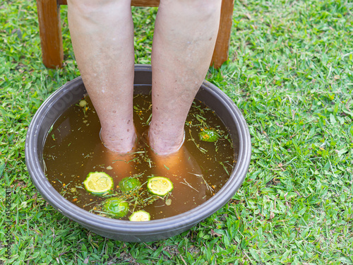 Close-up of the foot spa with herbs water for relaxation treatment. A senior woman who has ankle pain uses herbal treatment to relax the muscles by soaking warm water that is boiled from herbs photo