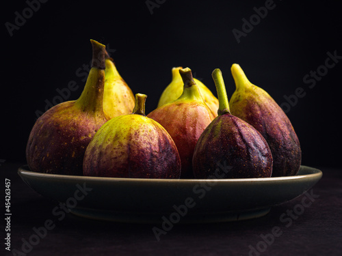 Pile of ripe figs fruit are on a plate with black background. High Vitamins fruit. Close-up photo. Healthy fruits and healthcare concept