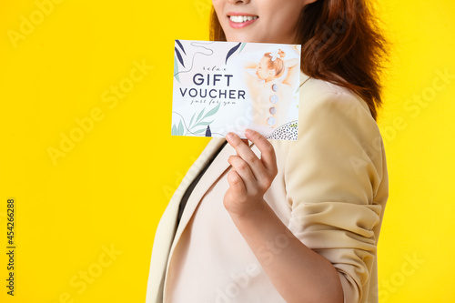 Young woman with gift voucher for massage on color background
