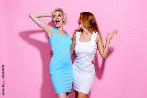 Two stunning beautiful confident lady chic hugging wearing pretty nice cute dresses isolated on pink studio background