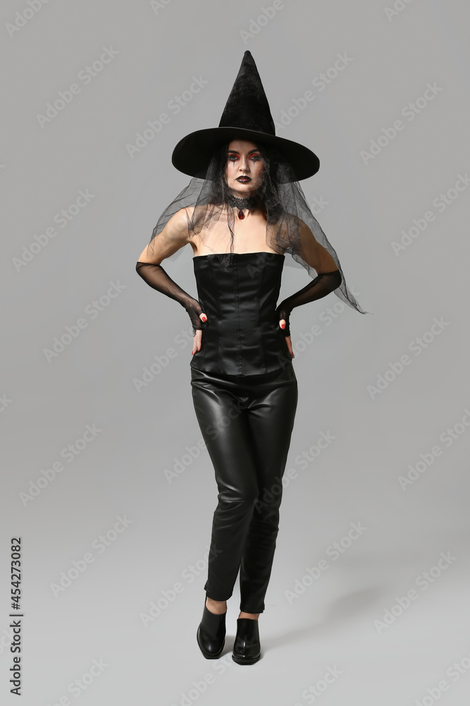 Beautiful woman dressed as witch for Halloween on grey background Beautiful woman dressed as witch for Halloween on grey background