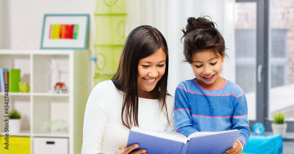 family, education and school concept - happy mother and daughter reading book over home background family, education and school concept - happy mother and daughter reading book over home background