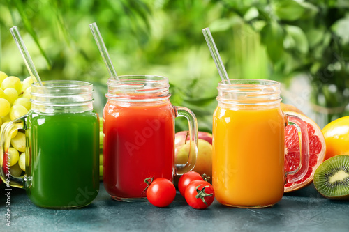Mason jars with healthy juice, fruits and vegetables on table outdoors