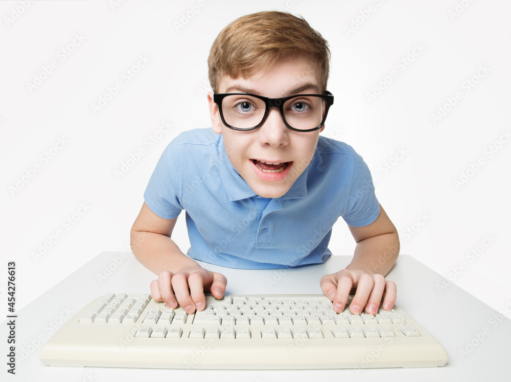 Surprised Child using Computer Keyboard. Teenage Boy Hacker typing on Laptop. Funny Kid In Eye Glasses Study Programming Code over White Studio Background Surprised Child using Computer Keyboard. Teenage Boy Hacker typing on Laptop. Funny Kid In Eye Glasses Study Programming Code over White Studio Background