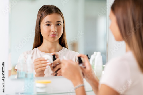 beauty, hygiene and people concept - teenage girl applying lotion to cotton disc at bathroom