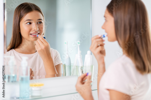 beauty and cosmetics concept - teenage girl applying lip balm and looking to mirror at home bathroom