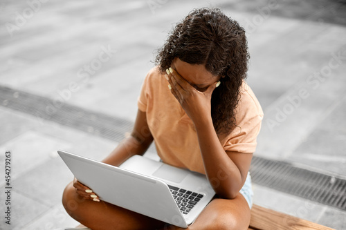 technology, education and people concept - stressed african american student girl with laptop computer in city photo