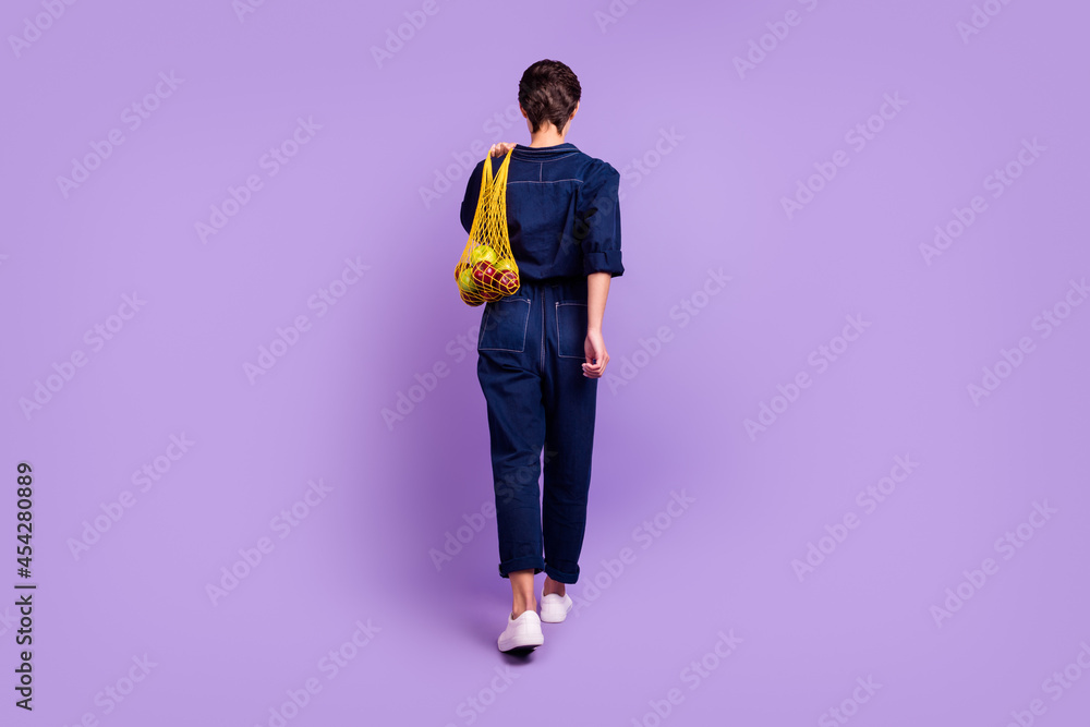 Full back view photo of charming woman go walk shopping use net reusable recycle bag isolated on purple color background Full back view photo of charming woman go walk shopping use net reusable recycle bag isolated on purple color background