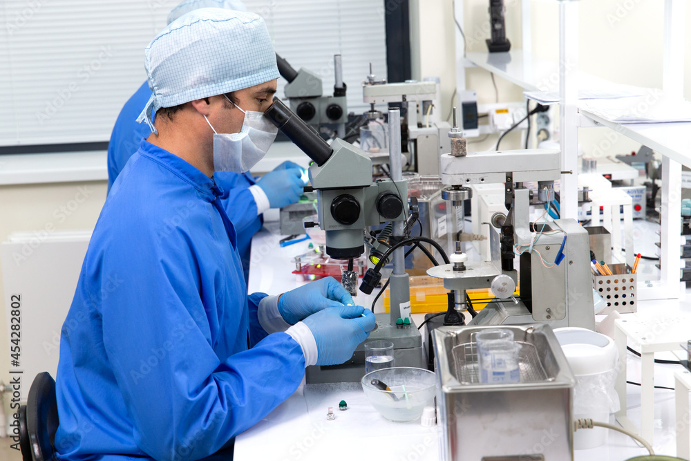 A male scientist in a mask looks through a microscope in a laboratory. A male scientist in a mask looks through a microscope in a laboratory.
