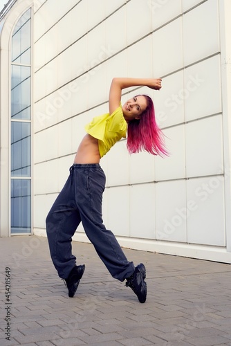 Fototapeta Naklejka Na Ścianę i Meble -  girl in full-length sportswear rose on her toes, dances and trains against background of building