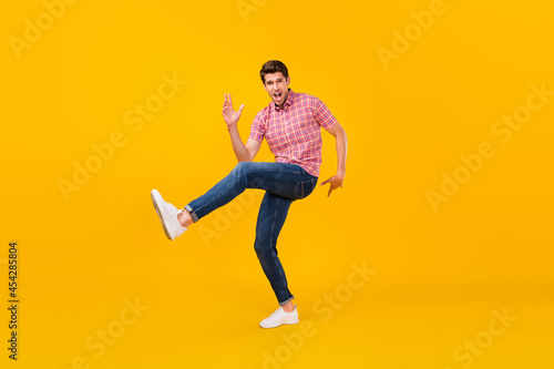 Full size photo of happy cheerful crazy man dance funky raise leg funny isolated on yellow color background © deagreez