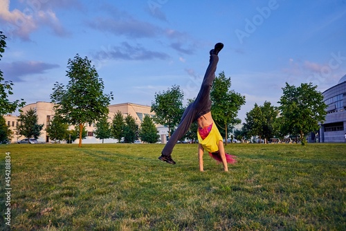 beautiful young girl with dyed pink hair, yellow crop top trains handspring in a city park photo