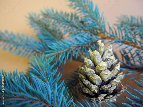 a cone painted in gold color lies on the branches of a blue Christmas tree on a beige table. side view