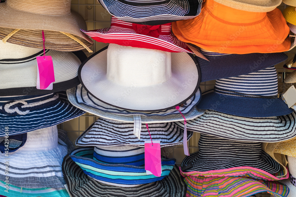 A variety of fashionable and colorful hats hanging on the window of a roadside store. Women's designer sun hats of different colors and styles.