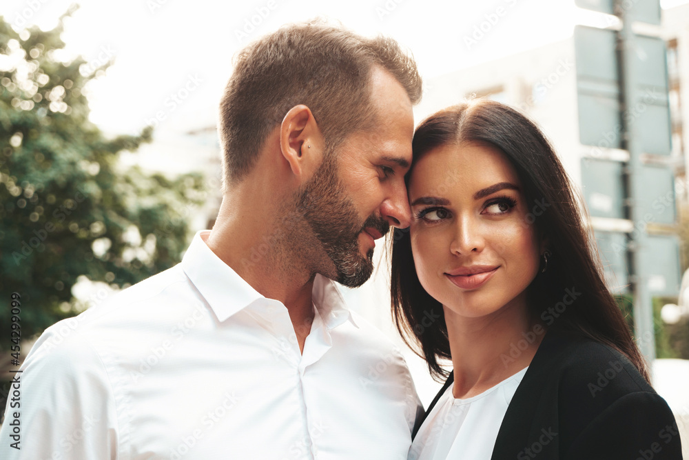 Beautiful fashion woman and her handsome boyfriend in suit. Sexy smiling brunette model in black evening dress. Fashionable couple posing in the street at sunset. Brutal man and his female outdoors Beautiful fashion woman and her handsome boyfriend in suit. Sexy smiling brunette model in black evening dress. Fashionable couple posing in the street at sunset. Brutal man and his female outdoors