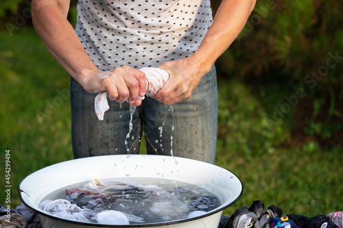 Woman wrings out underwear to an old basin outdoors in summer