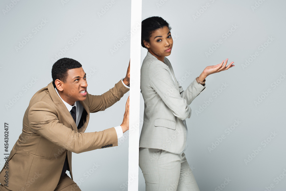 angry african american businessman pulling wall near pensive businesswoman on grey angry african american businessman pulling wall near pensive businesswoman on grey