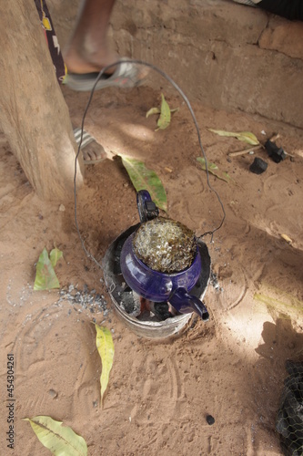 object closeup : aerial horizontal photography of a small blue kettle standing on a burning coal, with attaya tea boiling inside, outdoors on a sunny day in the Gambia, Africa photo