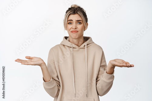 I dont know. Young confused woman shrugging shoulders, holding empty hands sideways, nothing to offer, standing against white background photo