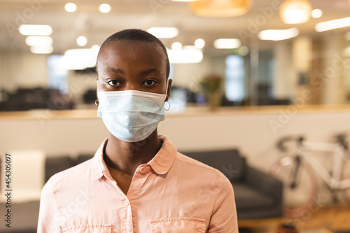 Portrait of african american female creative wearing face mask at work, looking to camera photo