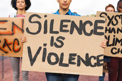 Mixed race woman holding placard saying silence is violence at protest march photo