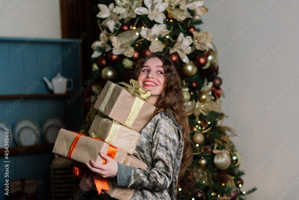 Young smiling woman in sweater, winter holidays in decorated home interior with Christmas tree.