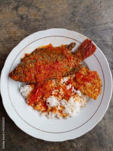 Fish dishes from Indonesia. Bali mujair is tilapia cooked with red chili and tomatoes. Besides tilapia fish, tempeh is also added as a mixture. Isolated on the background of an ancient cement floor. photo