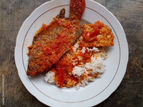 Fish dishes from Indonesia. Bali mujair is tilapia cooked with red chili and tomatoes. Besides tilapia fish, tempeh is also added as a mixture. Isolated on the background of an ancient cement floor. photo
