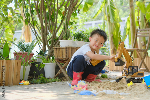 Cute Asian young boy playing with sand alone at home, Kid playing with sand toys and toy construction machinery in backyard home garden , Montessori education, Creative play for kids concept