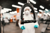 The serious situation with the corona virus. Suppression of COVID-19 virus and cleaning of exercise equipment in the gym by a male person in a protective white suit