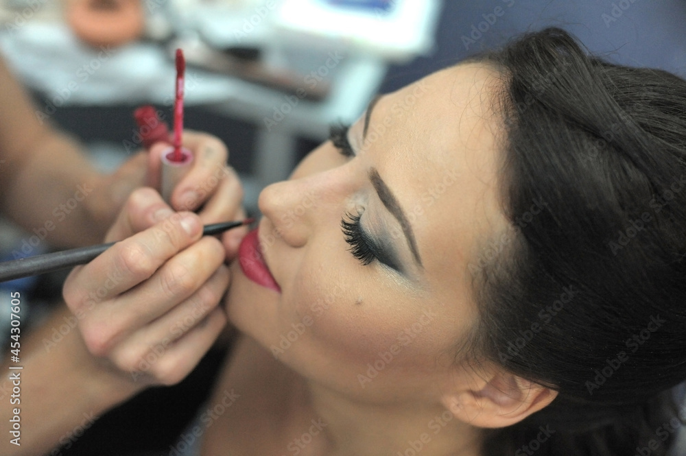 Wedding makeup artist making a make up for bride. Beautiful woman model with curly hair indoors. Female portrait. Close-up hands near face. Young beautiful girl applying make-up by make-up artist Wedding makeup artist making a make up for bride. Beautiful woman model with curly hair indoors. Female portrait. Close-up hands near face. Young beautiful girl applying make-up by make-up artist