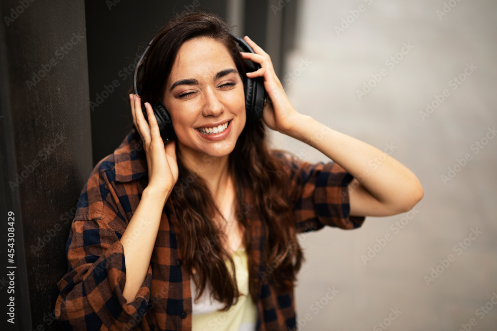 Young smiling woman with headphones outdoors. Beautiful happy girl listening the music. Young smiling woman with headphones outdoors. Beautiful happy girl listening the music.
