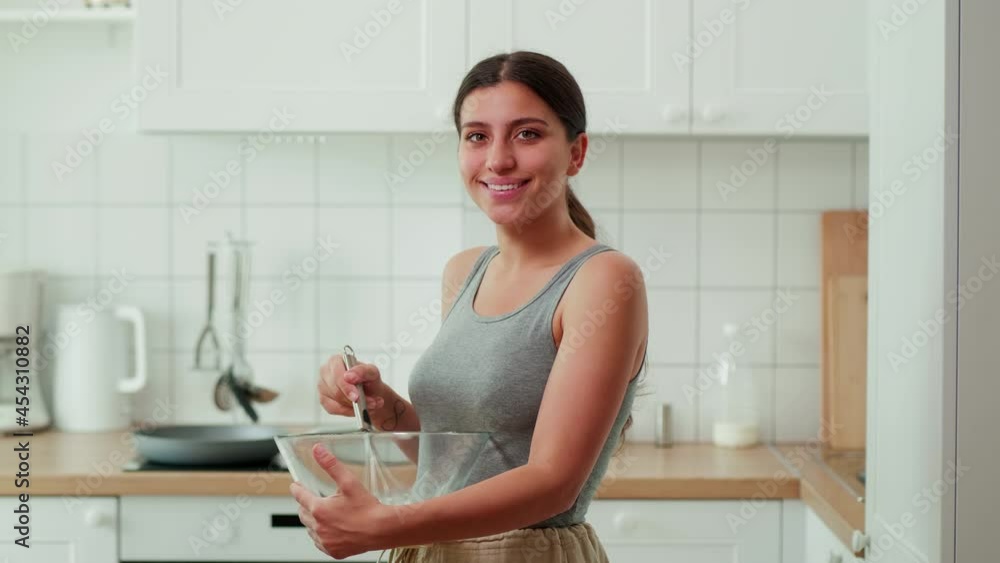 girl whips food with a whisk holding a plate in her hands.Looks at the camera and smiles. Medium plan. High quality 4k footage girl whips food with a whisk holding a plate in her hands.Looks at the camera and smiles. Medium plan. High quality 4k footage