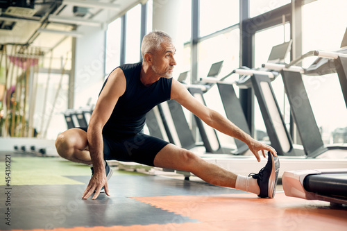 Fototapeta Naklejka Na Ścianę i Meble -  Mature sportsman stretches his leg while warming up in gym.