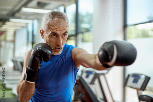 Mature man exercises boxing during sports training at gym. © Drazen