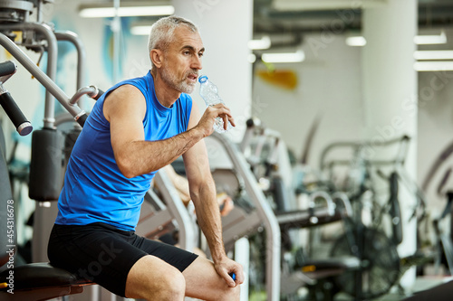 Mature athletic man drinking water on break during sports training at gym.