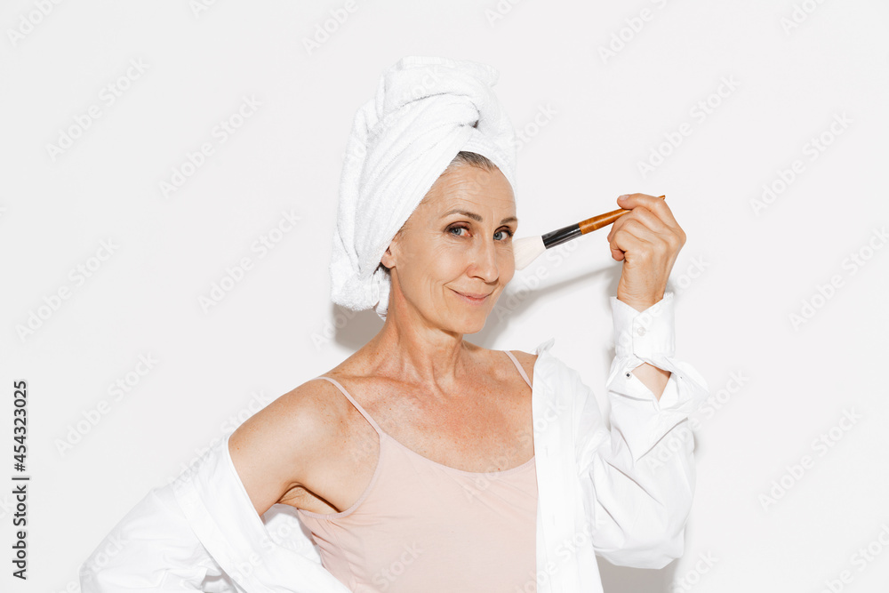 Senior woman wrapped in towel smiling while using powder brush Senior woman wrapped in towel smiling while using powder brush