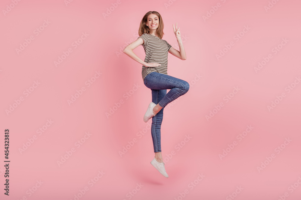 Full length profile side photo of young woman happy positive smile show peace cool v-sign jump up isolated over pink color background