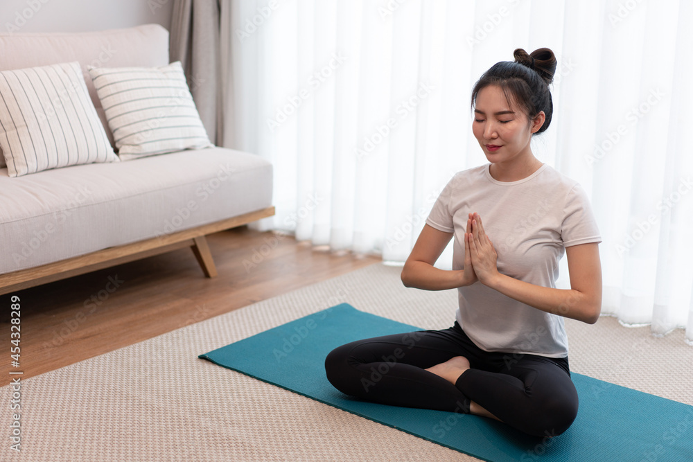 Fototapeta premium Productive activity concept a female young adult closing her eyes putting her hands together on the green mat in the quiet room