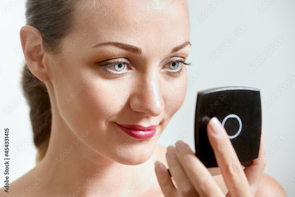 Beautiful woman checking her makeup in mirror on white background Beautiful woman checking her makeup in mirror on white background
