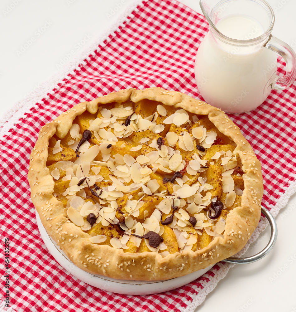 baked round pie with apple pieces, sprinkled with almond flakes on a white table baked round pie with apple pieces, sprinkled with almond flakes on a white table