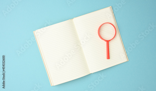 paper notebook with blank white sheets and a red magnifier on a blue background. Background for inscriptions