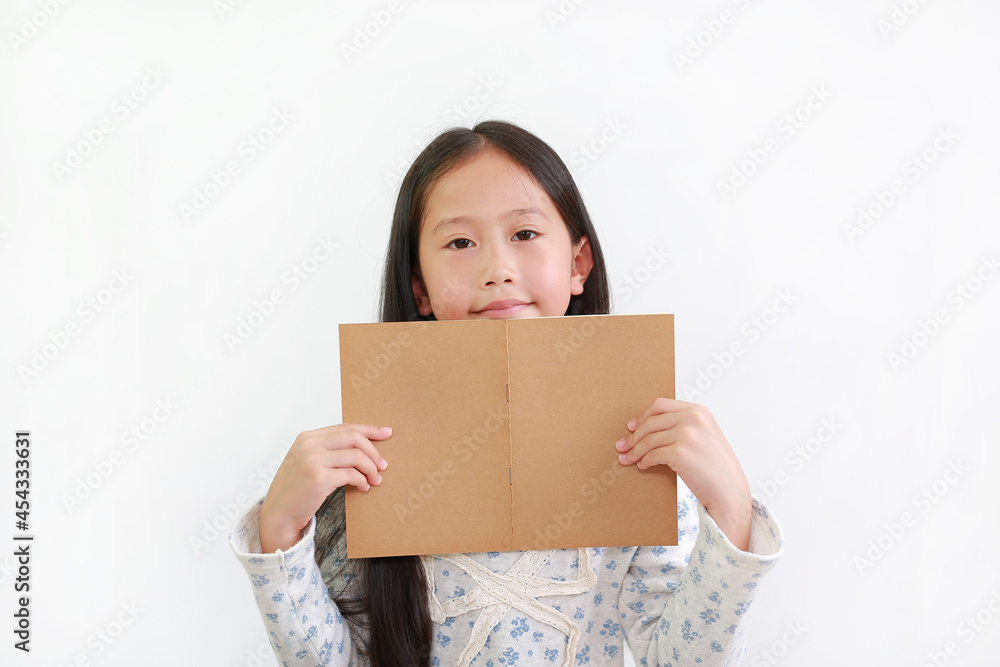 Happy Asian little girl child holding open brown book with looking at camera over white studio background Happy Asian little girl child holding open brown book with looking at camera over white studio background