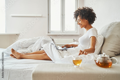 Joyous attractive woman checking email in bed