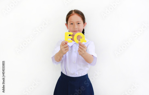 Asian little girl child in school uniform holding alphabet EQ (Emotional Quotient) text on her face over white background. Education concept. Focus at text in hands