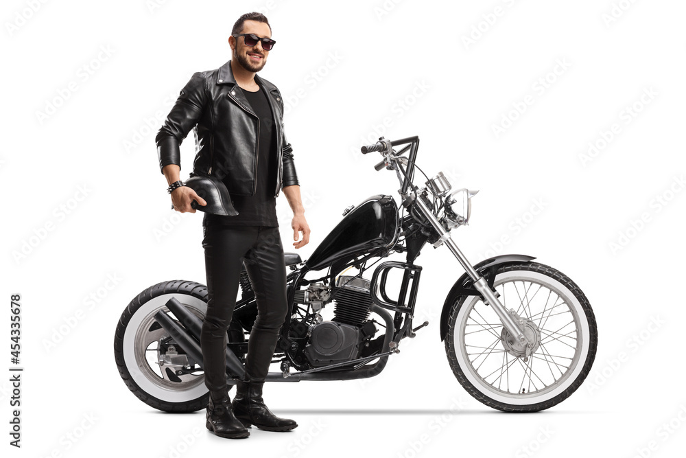 Naklejka premium Full length portrait of a biker with a chopper holding helmet and wearing sunglasses