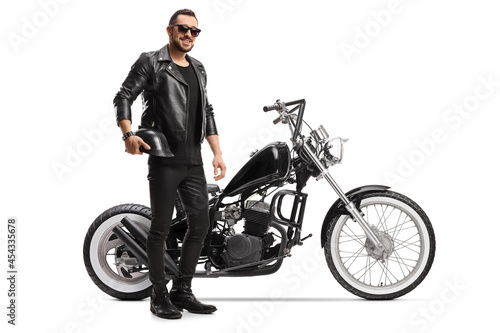 Full length portrait of a biker with a chopper holding helmet and wearing sunglasses