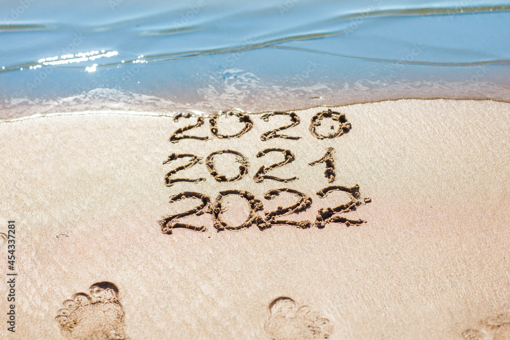Fototapeta premium The numbers 2021, 2022 are drawn on the sand and washed away by the wave, the symbol of the new year, the change of the year